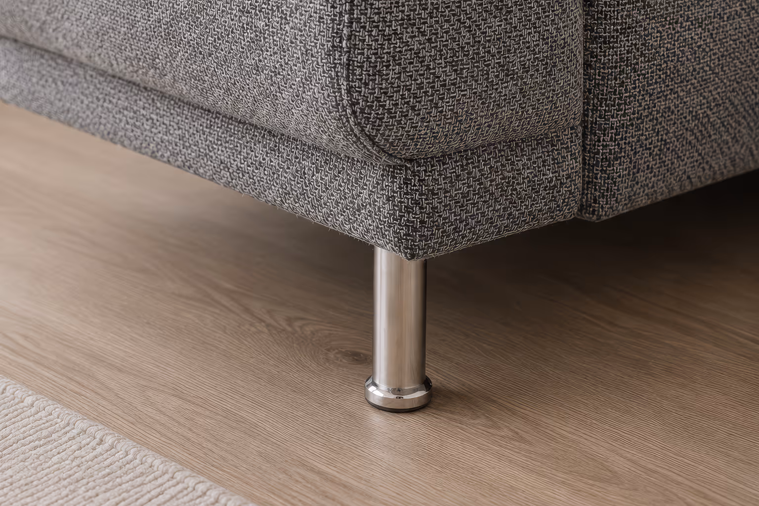 Close-up of a gray textured sofa corner with a metal leg on a wooden floor near a light rug.
