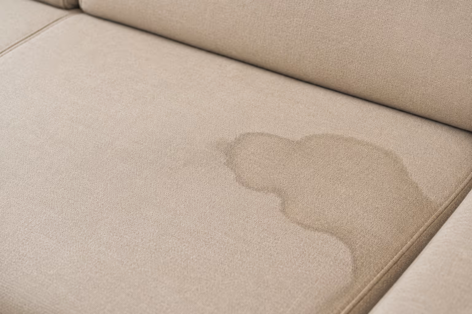 Beige fabric couch cushion with a noticeable wet stain near the corner.