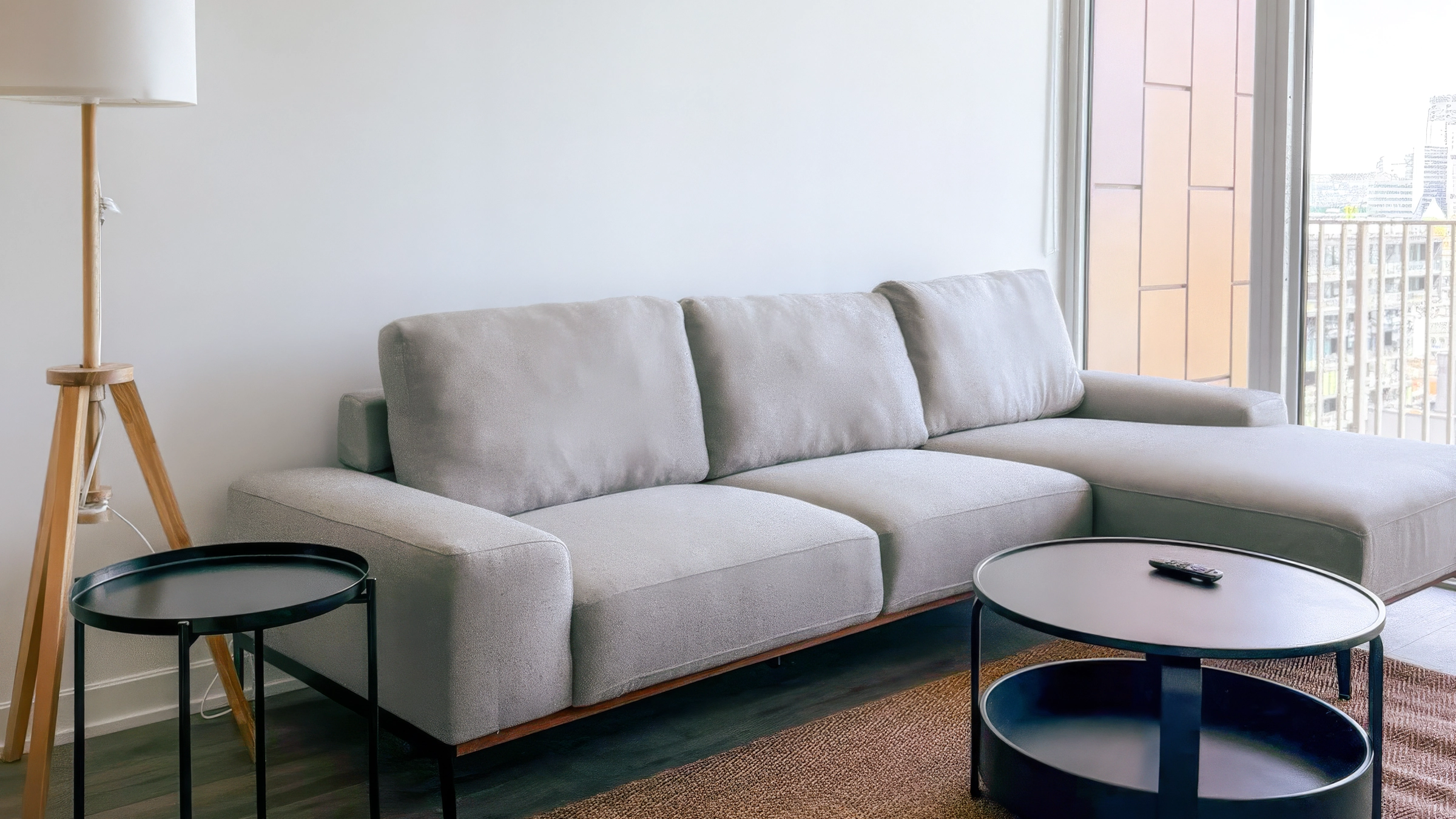 Modern living room with gray sectional sofa, wooden floor lamp, black round tables, and balcony door.