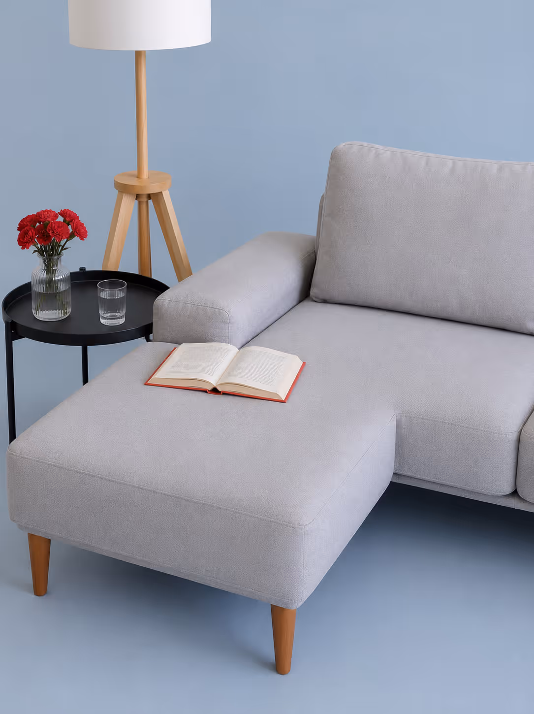 Light gray sofa with an open book on the chaise, next to a black side table with red flowers and a glass.