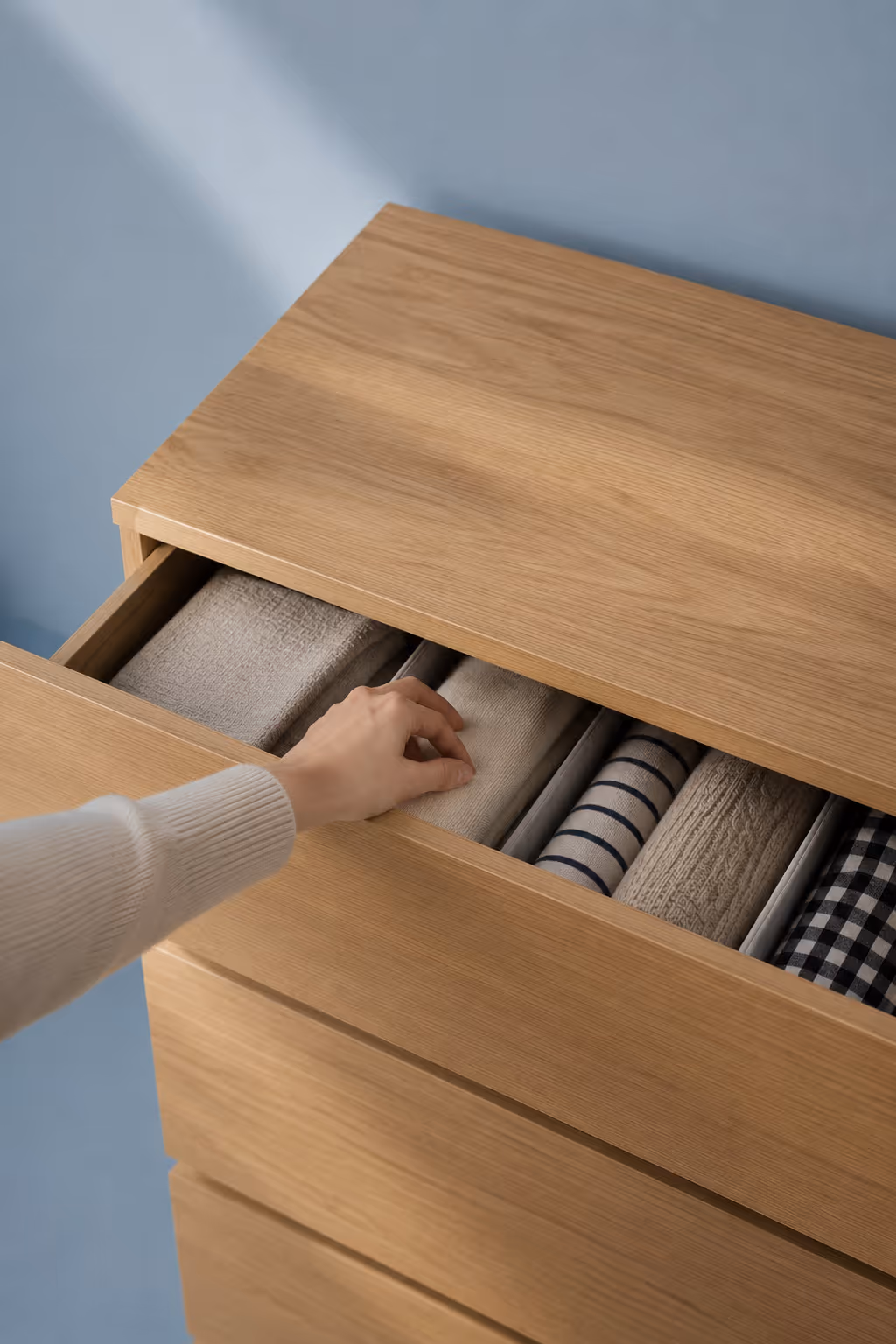 Hand organizing folded clothes in a neatly divided drawer of a wooden chest.