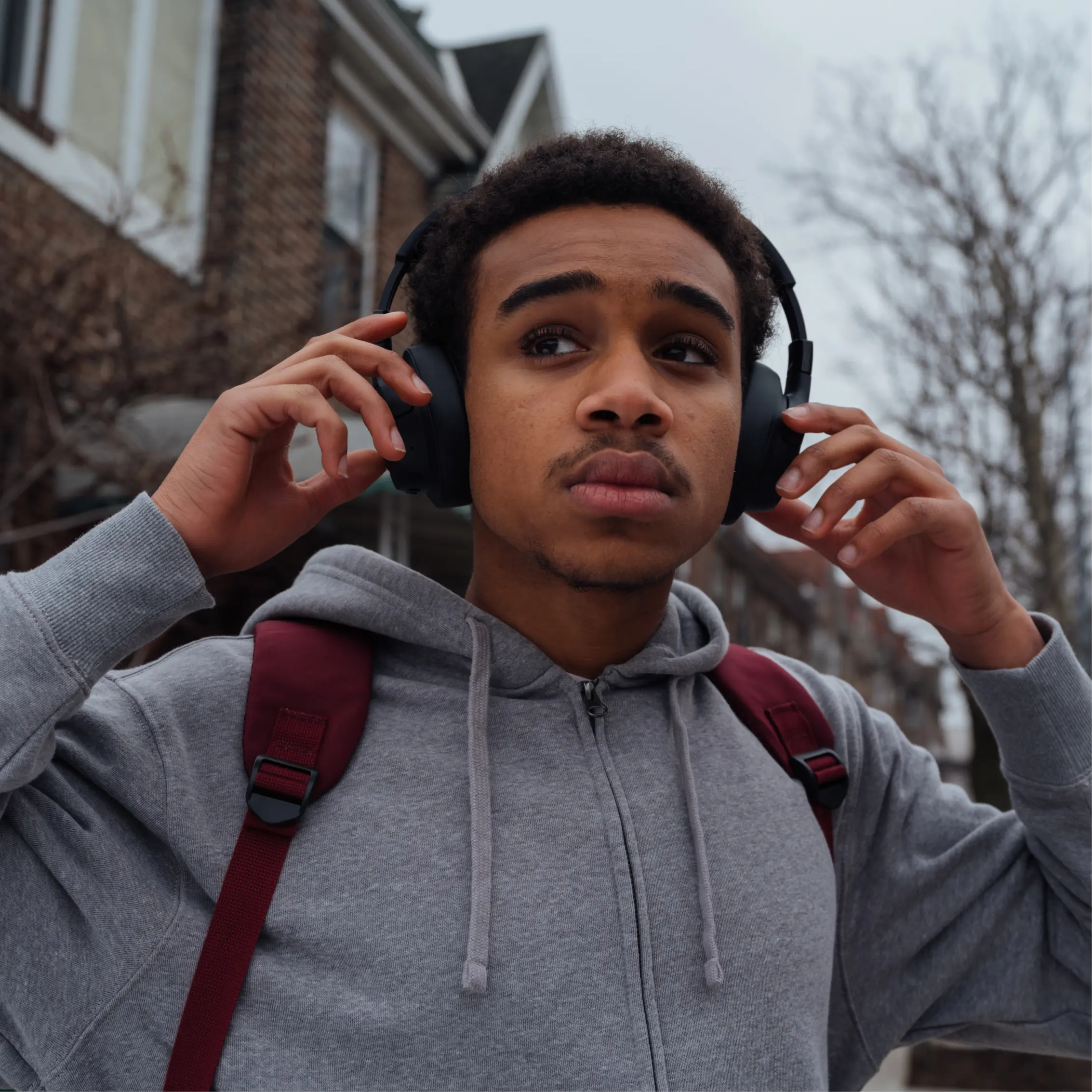 Young man in gray hoodie and red book bag with earphones