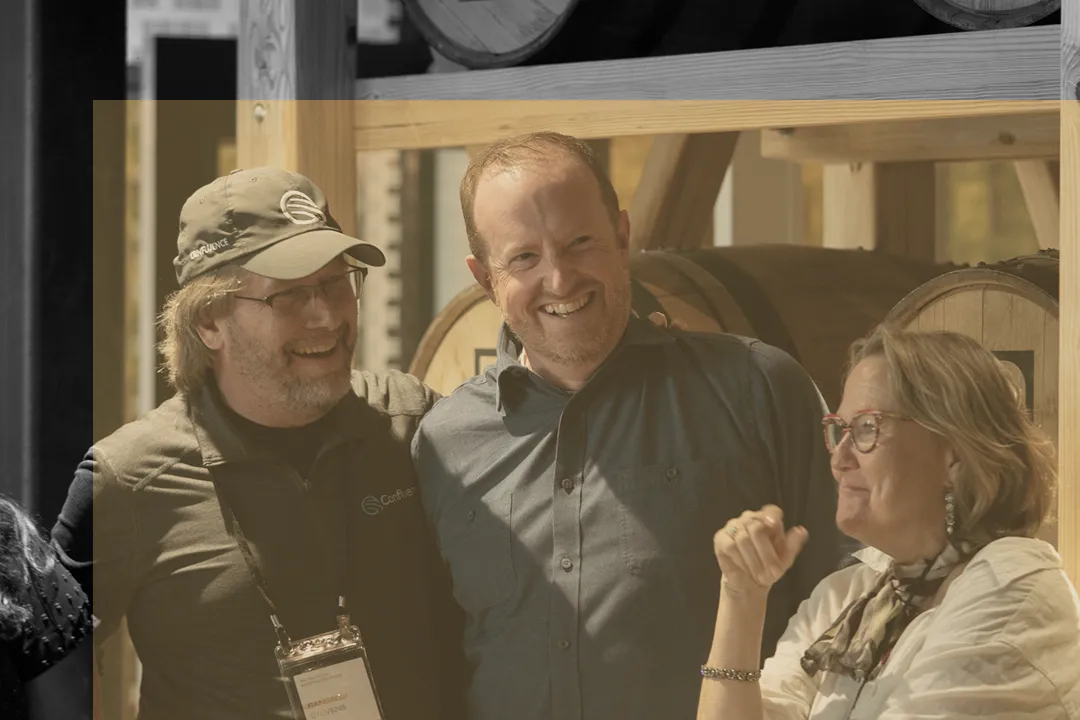 Three people smiling and talking at Confluence Lexington professional development event near wooden bourbon barrels
