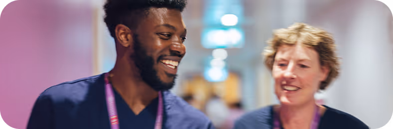 Two healthcare professionals, a man and a woman, smiling and walking together in a hospital corridor.