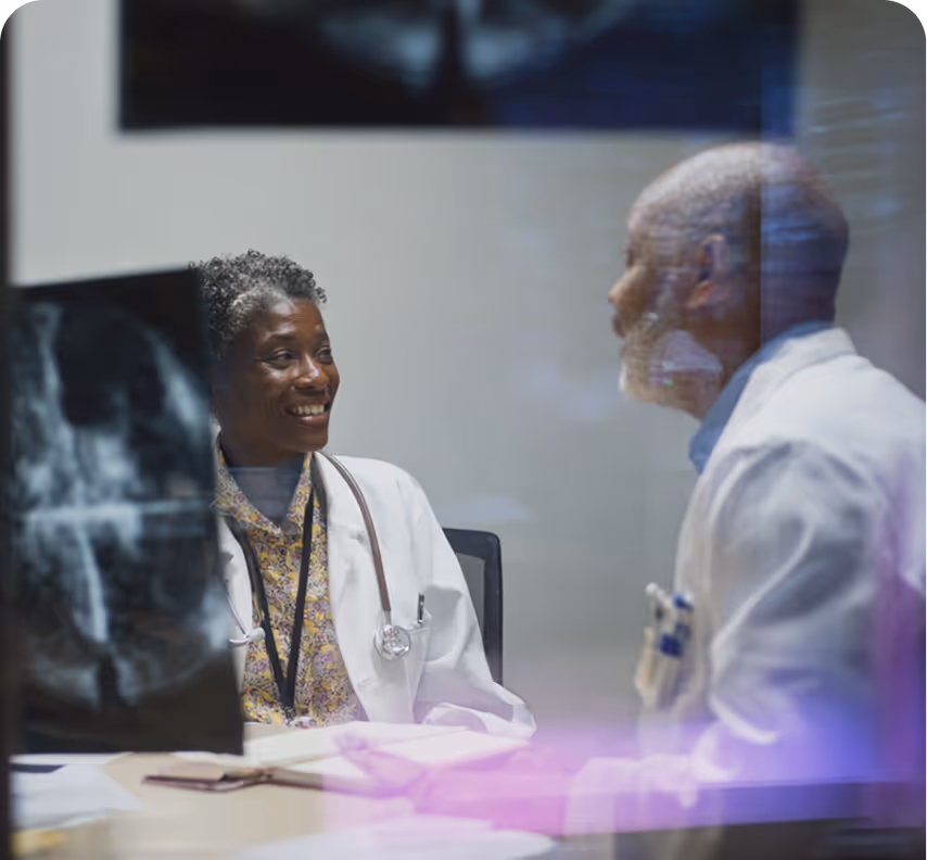 Two doctors in white coats discussing and smiling in an office with an X-ray image visible in the foreground.
