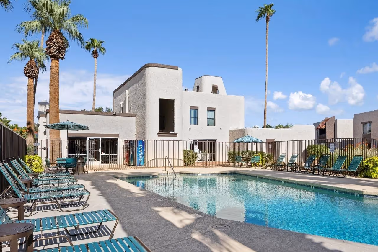 Swimming pool with palm trees, lounge chairs, and table with umbrella and view of exterior