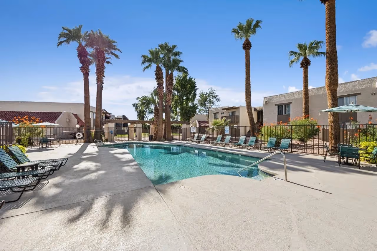 Swimming pool with palm trees, lounge chairs, and table with umbrella