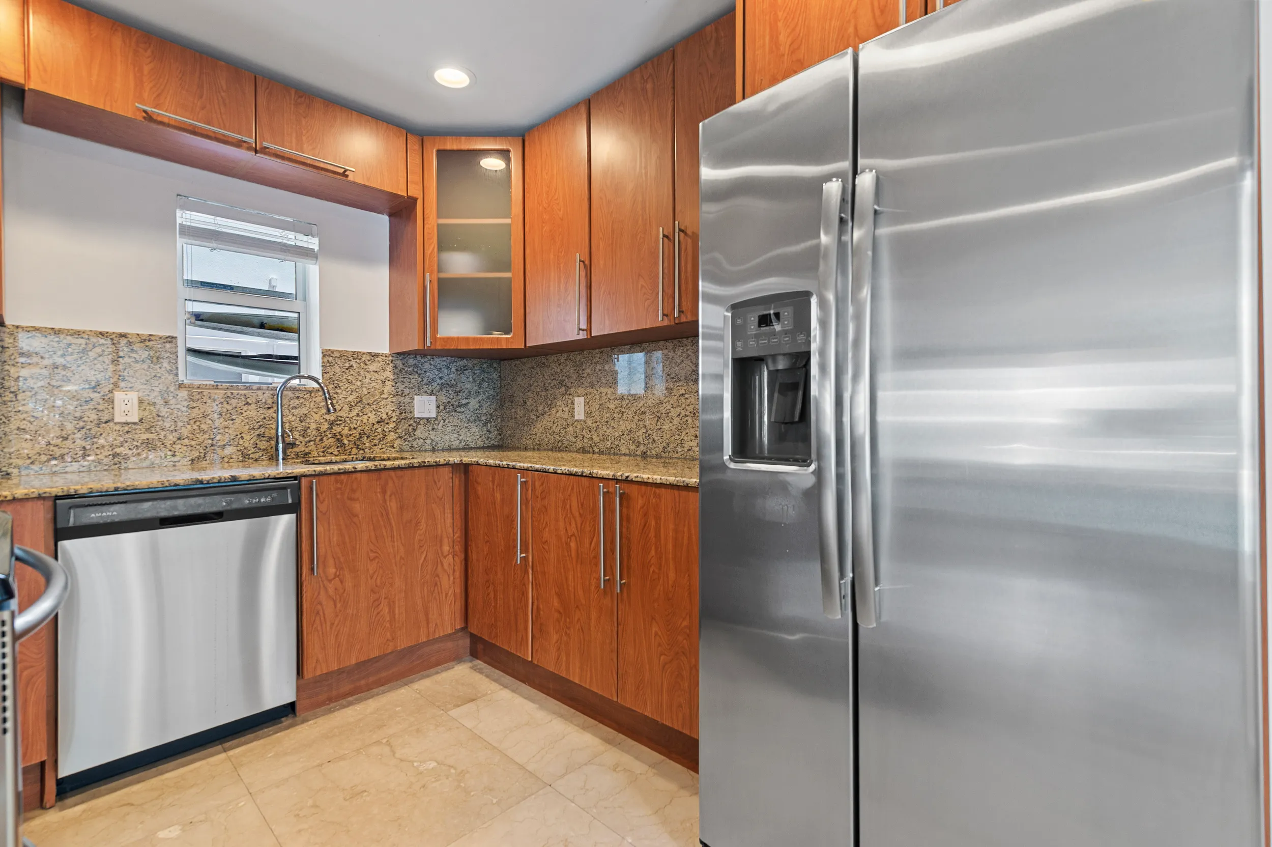 Modern kitchen corner with wooden cabinets, granite countertops, stainless steel dishwasher, and a large stainless steel refrigerator with water dispenser.