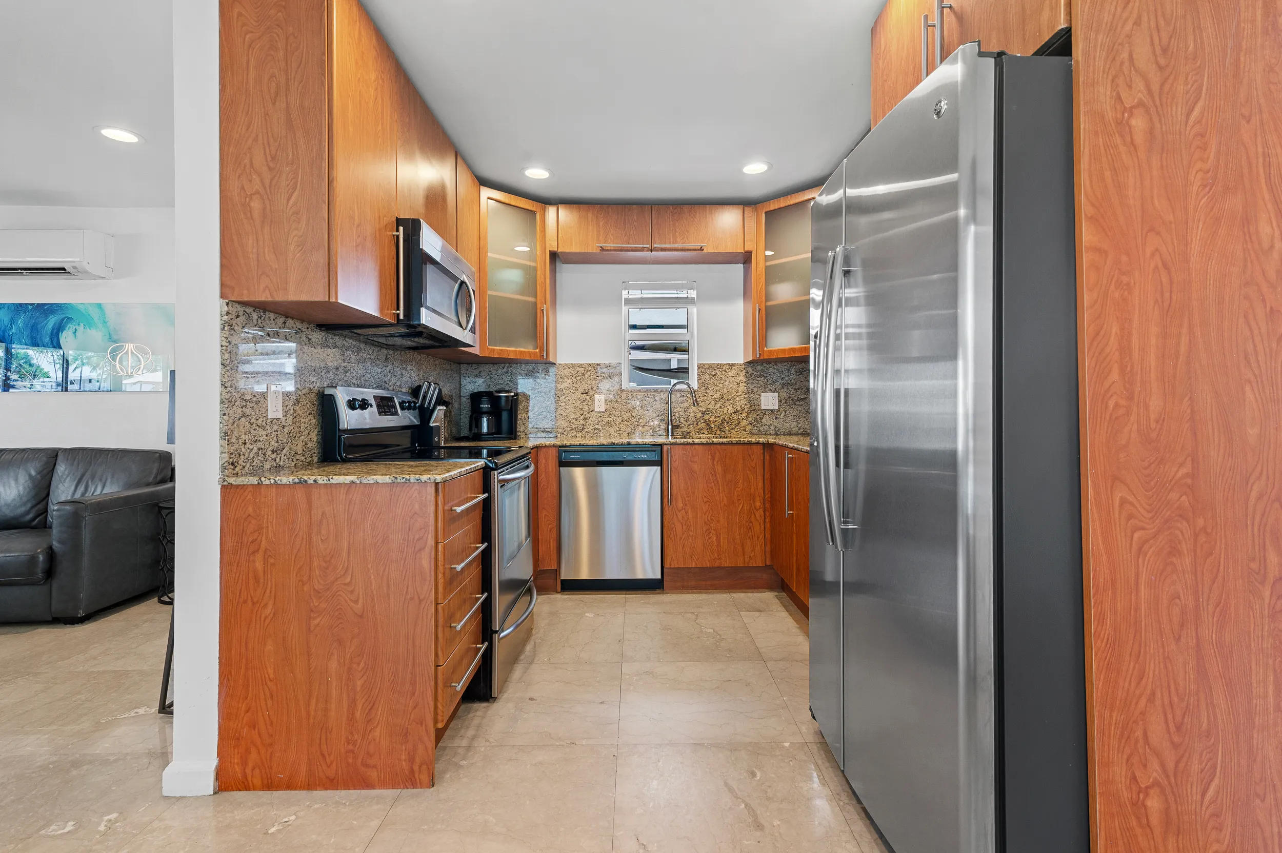 Modern kitchen with stainless steel appliances, wooden cabinets, granite countertops, and beige tiled floor.