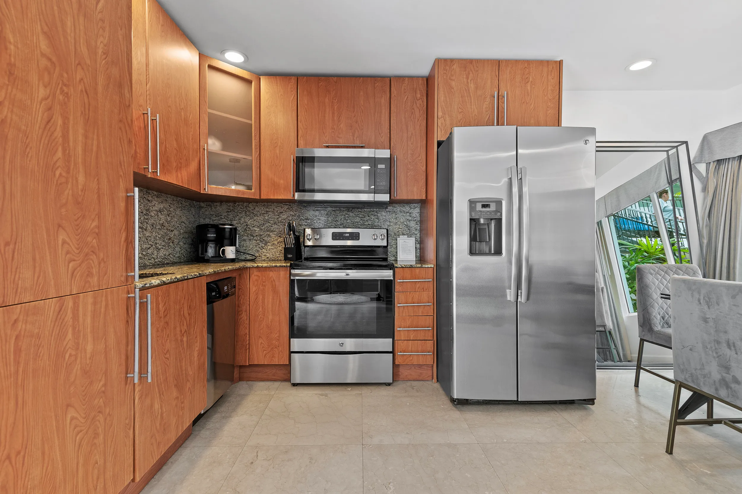 Modern kitchen with wood cabinets, stainless steel refrigerator, oven, microwave, dishwasher, and coffee maker.