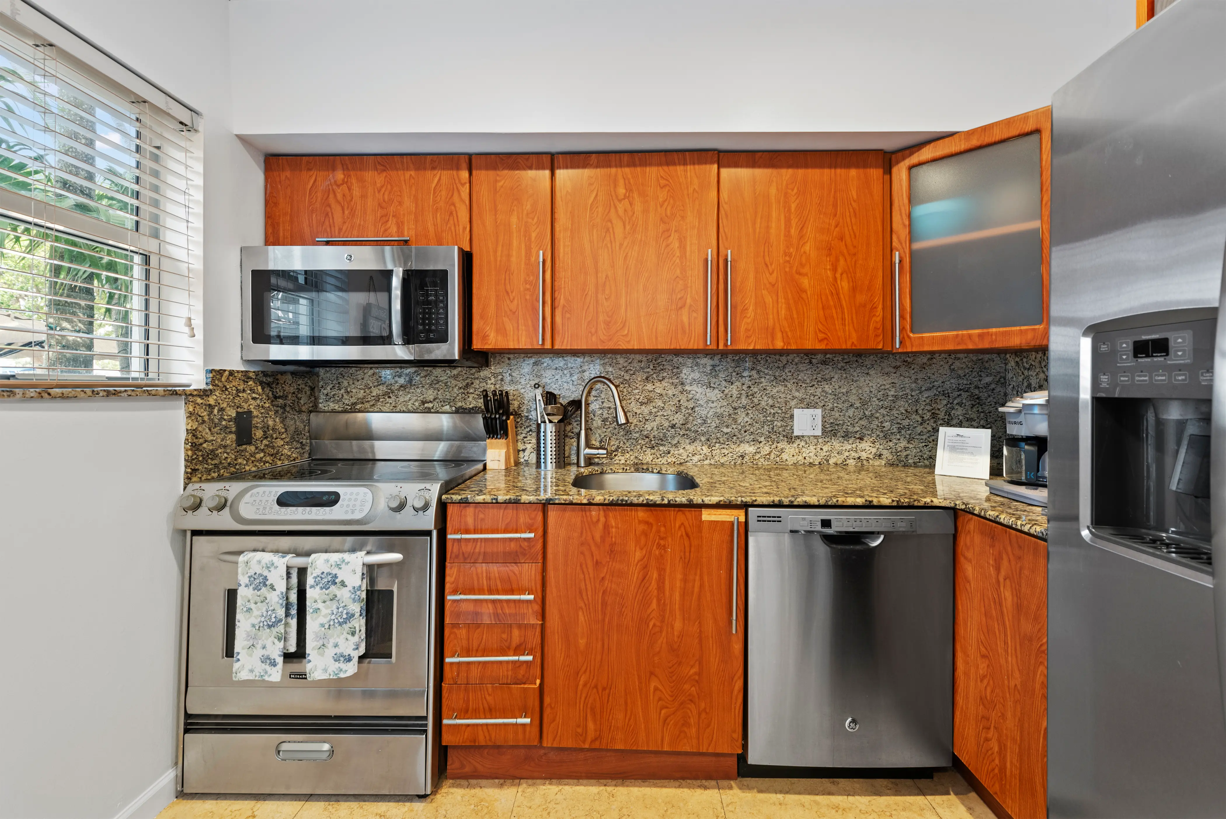 Modern kitchen with wooden cabinets, stainless steel appliances including microwave, stove, dishwasher, refrigerator, and a granite countertop with sink.