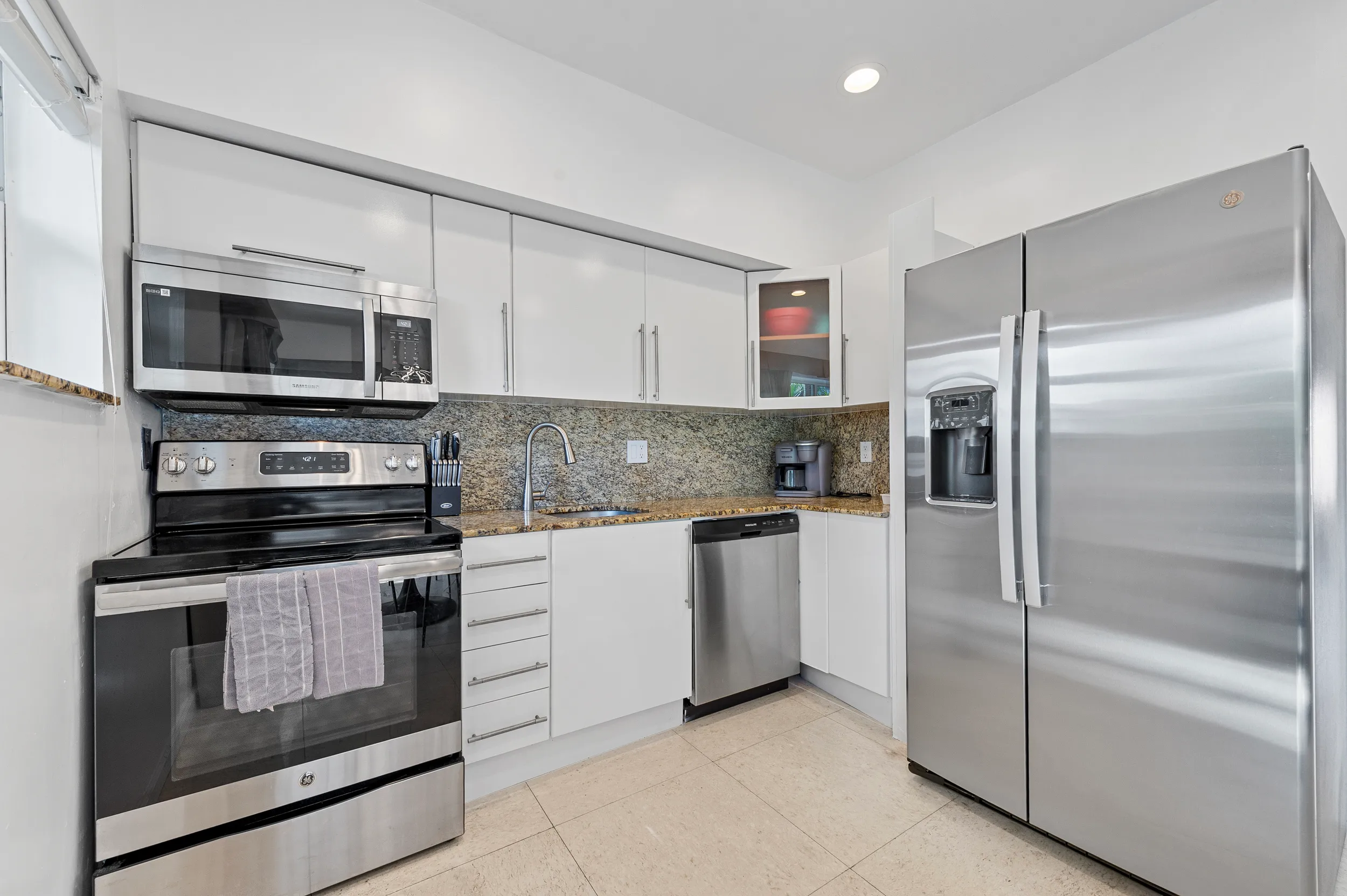 Modern kitchen with stainless steel appliances including a refrigerator, microwave, oven, and dishwasher, white cabinets, and granite countertops.