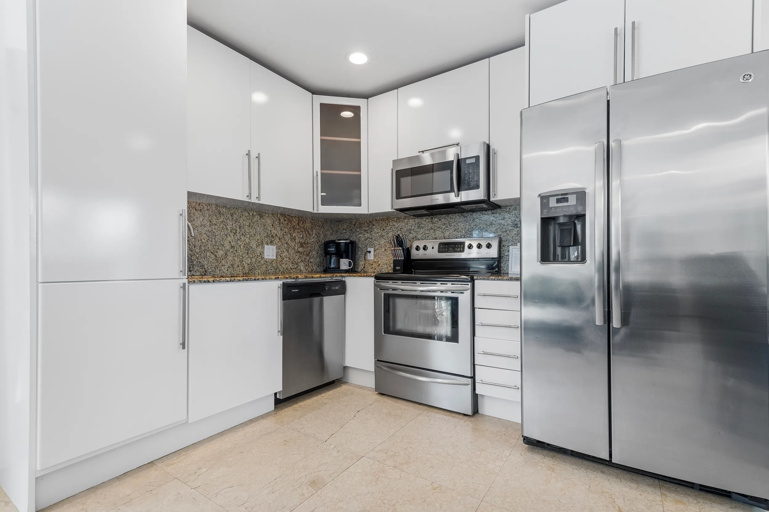 Modern kitchen with stainless steel refrigerator, oven, microwave, dishwasher, white cabinets, and granite countertops.
