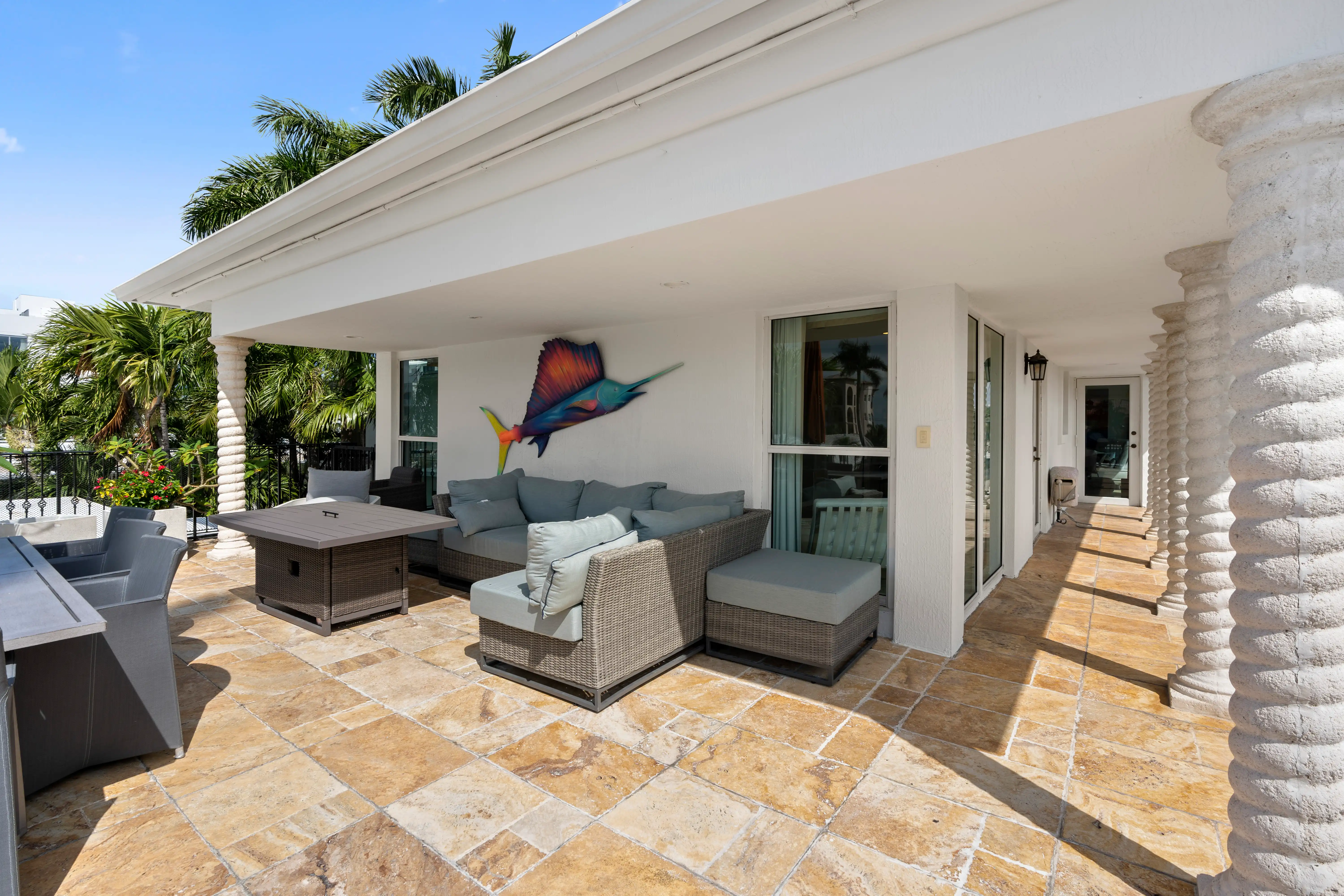 Outdoor covered patio with wicker sectional sofa, cushioned chairs, a table, and a colorful fish wall decoration.