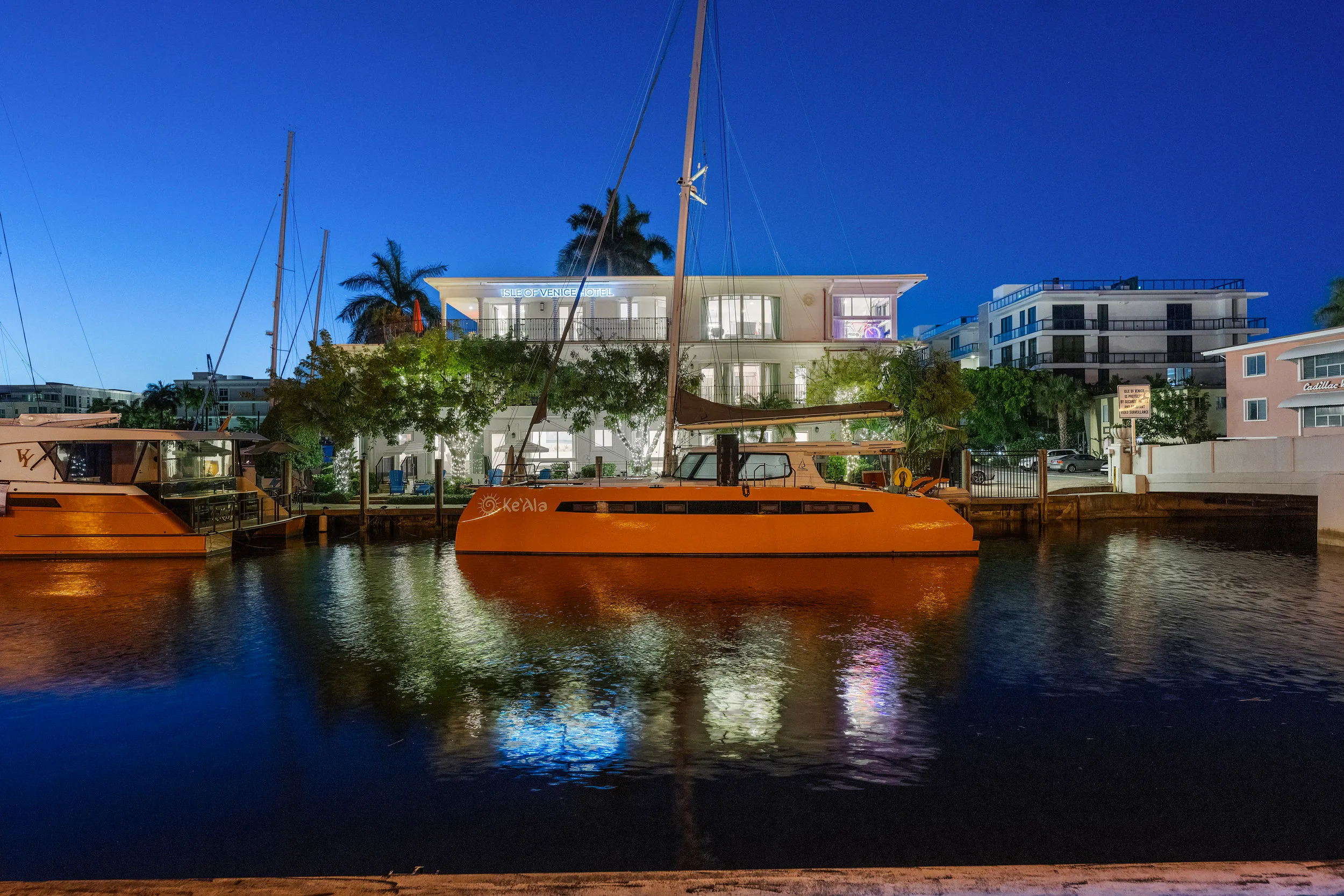 Orange sailboat named Ke'Ala docked in a canal at dusk with the Isle of Venice Hotel and city buildings in the background.