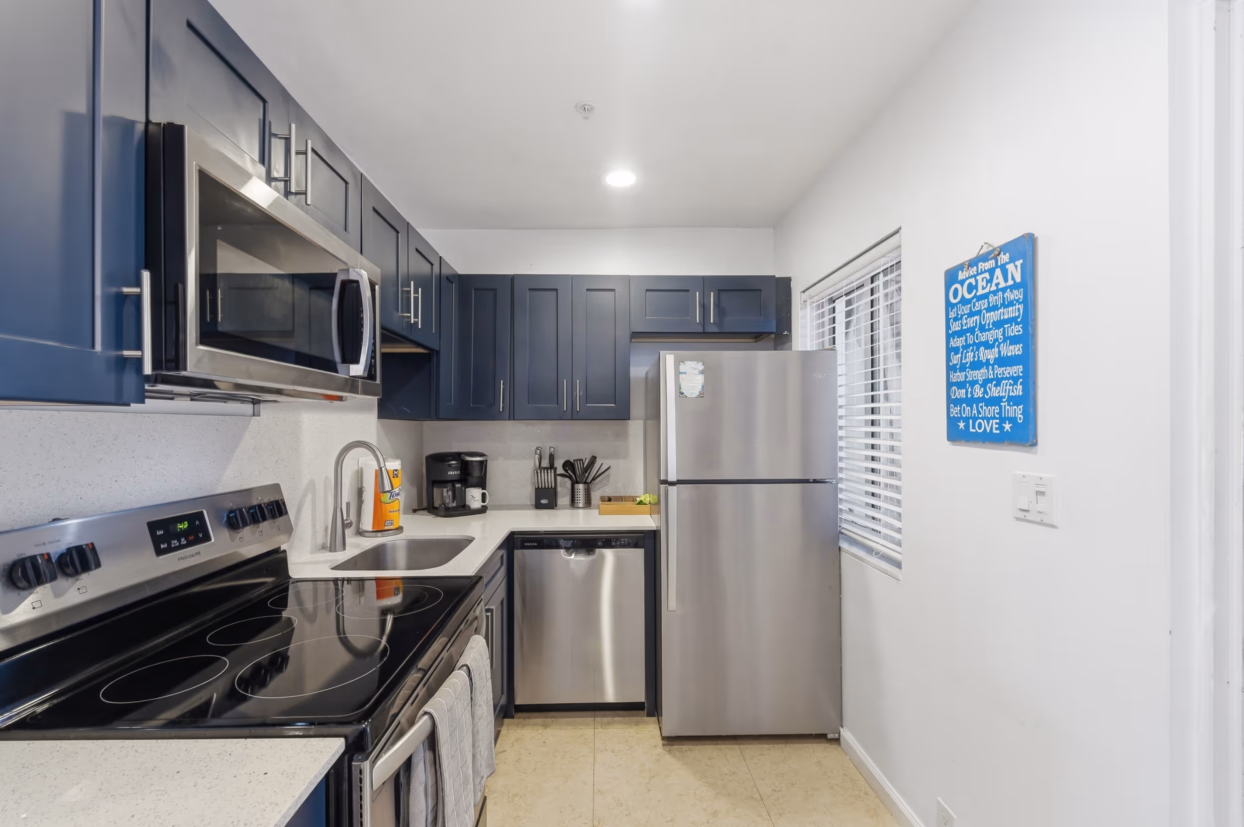 Modern kitchen with navy blue cabinets, stainless steel appliances, and a blue ocean-themed wall sign.