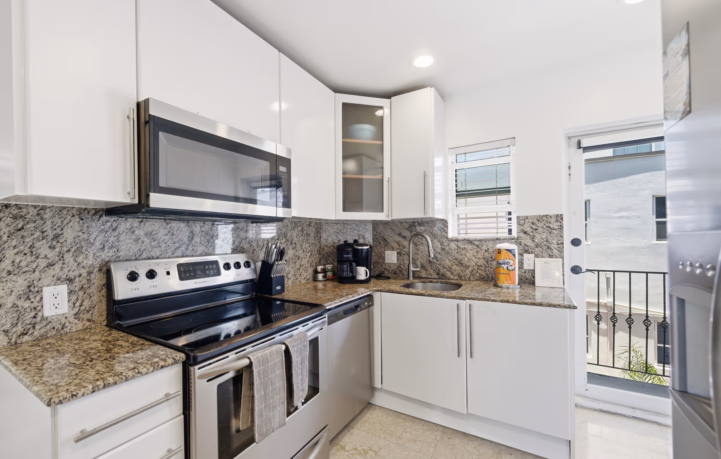 Modern kitchen with white cabinets, granite countertops, stainless steel appliances, and a small window.