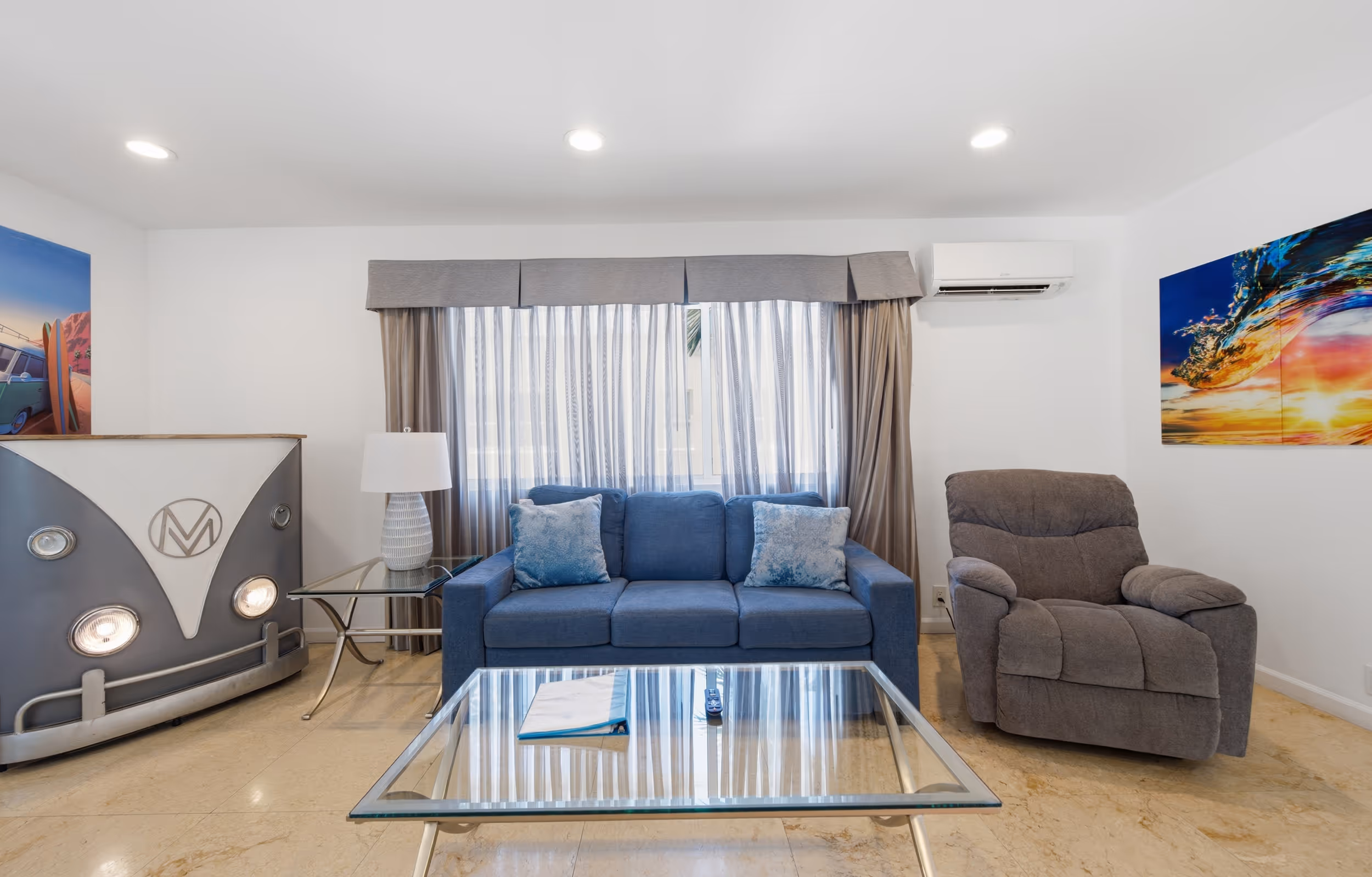 Living room with blue sofa, gray recliner, glass coffee table, and car-front shaped cabinet.