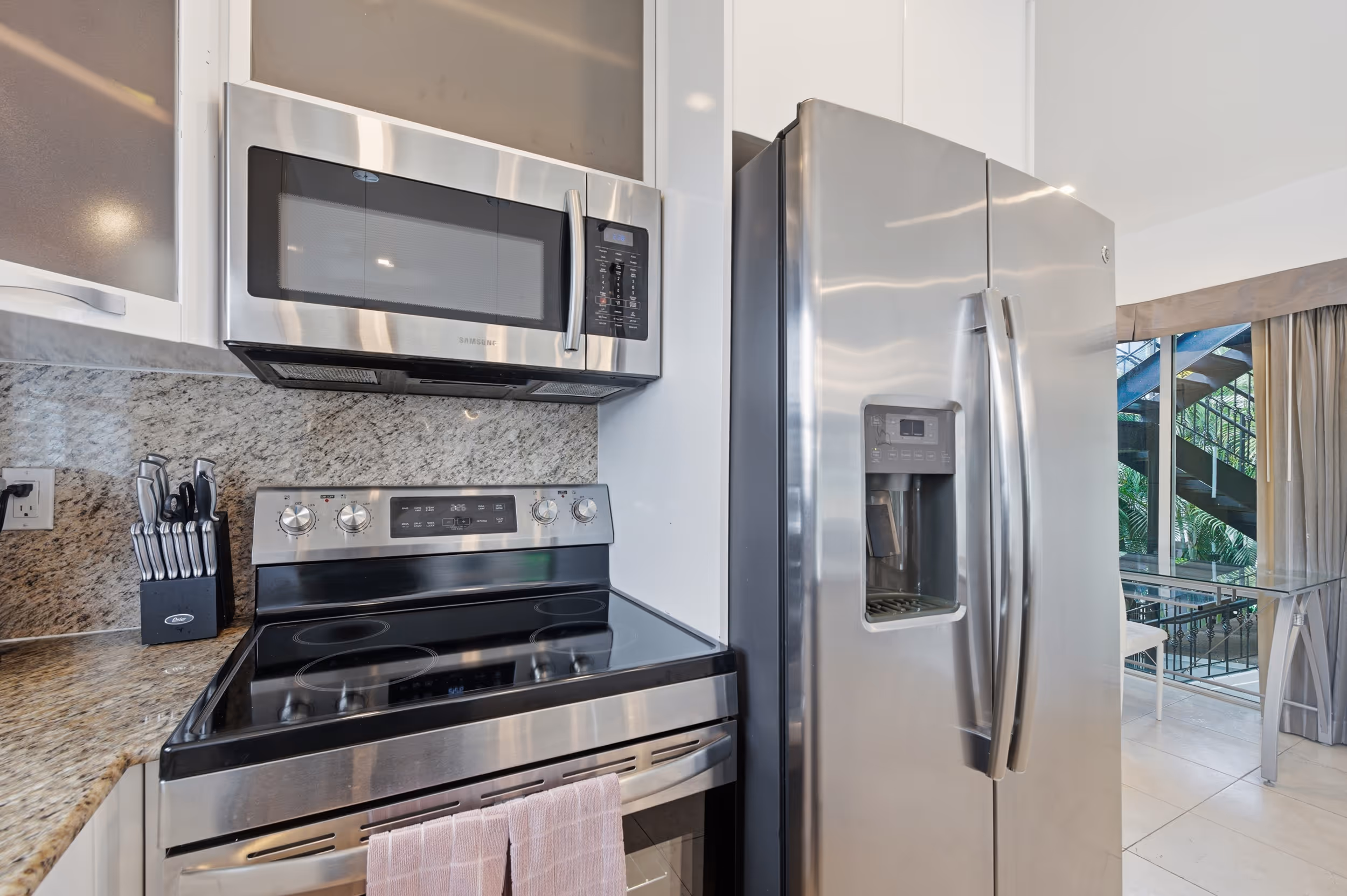 Modern kitchen with stainless steel microwave, electric stove, and side-by-side refrigerator with water dispenser.