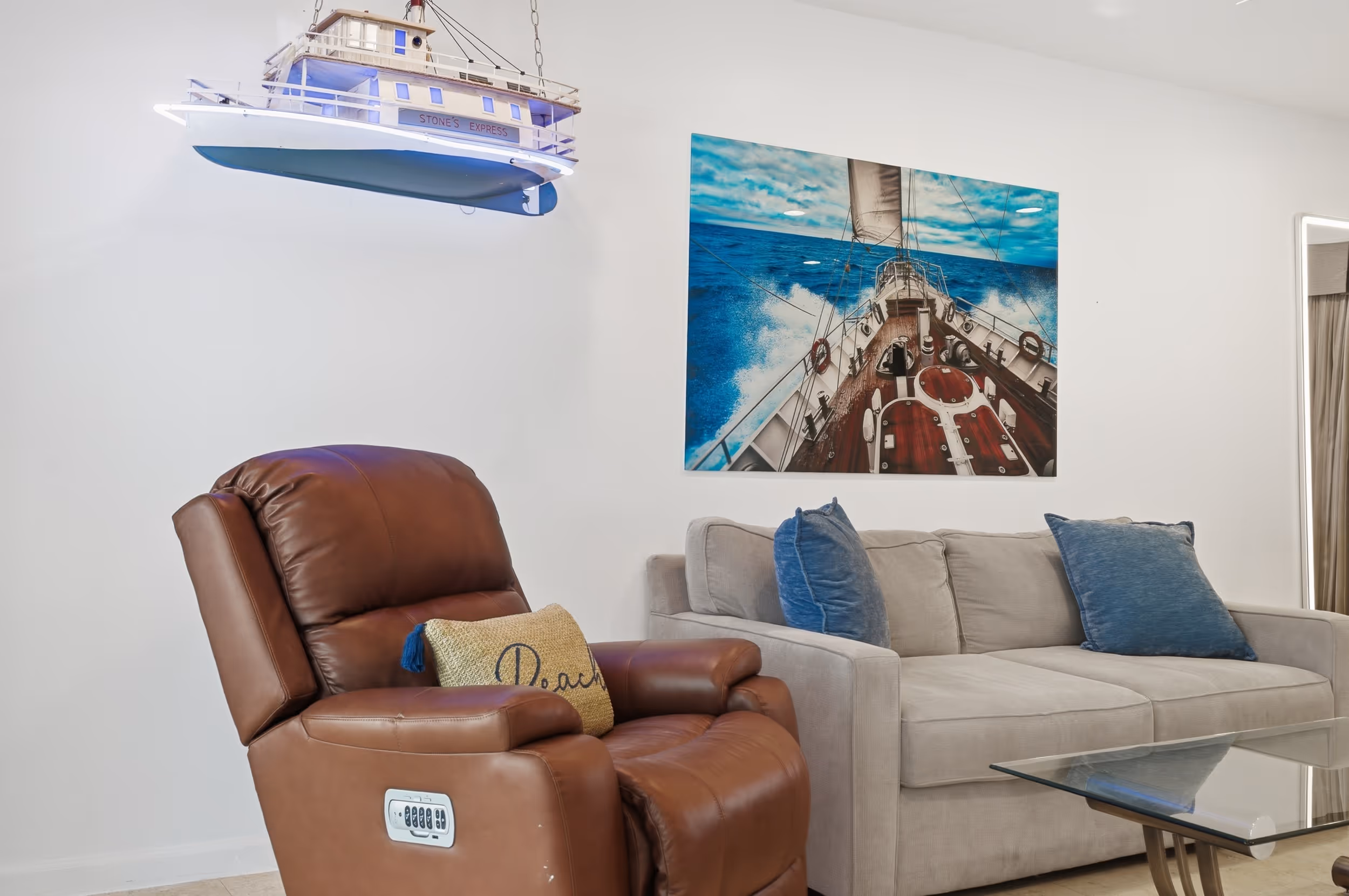Living room with brown recliner, gray sofa with blue pillows, boat wall lamp, and sailboat artwork.