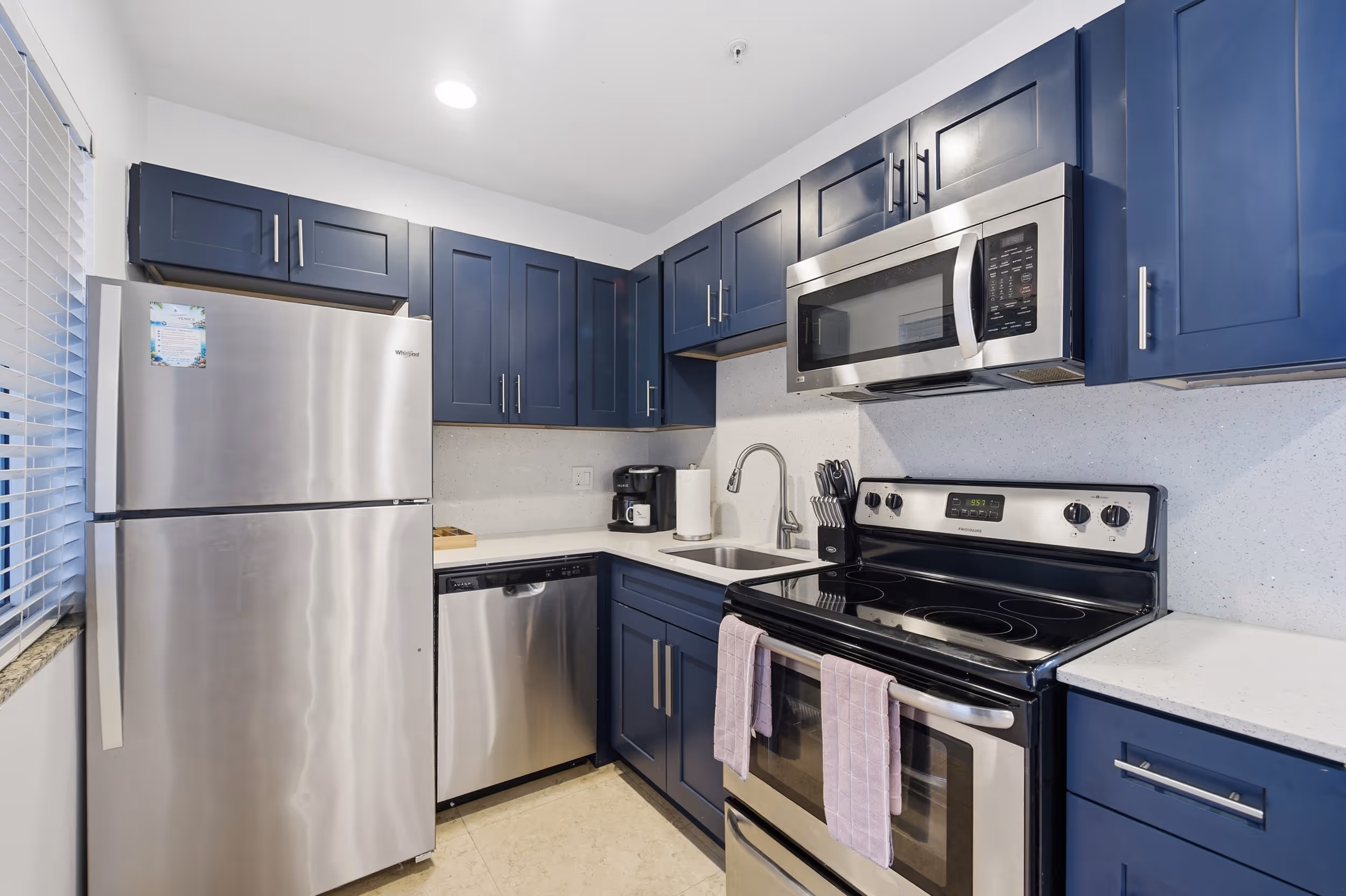 Modern kitchen with blue cabinets, stainless steel appliances, a sink, and two pink towels on the oven handle.