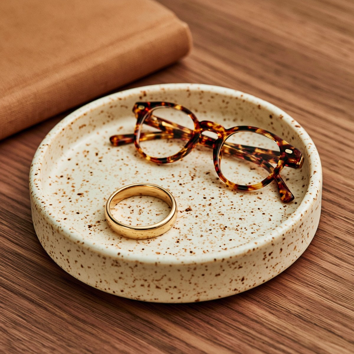 Small ceramic tray holding a ring and reading glasses on a wood nightstand