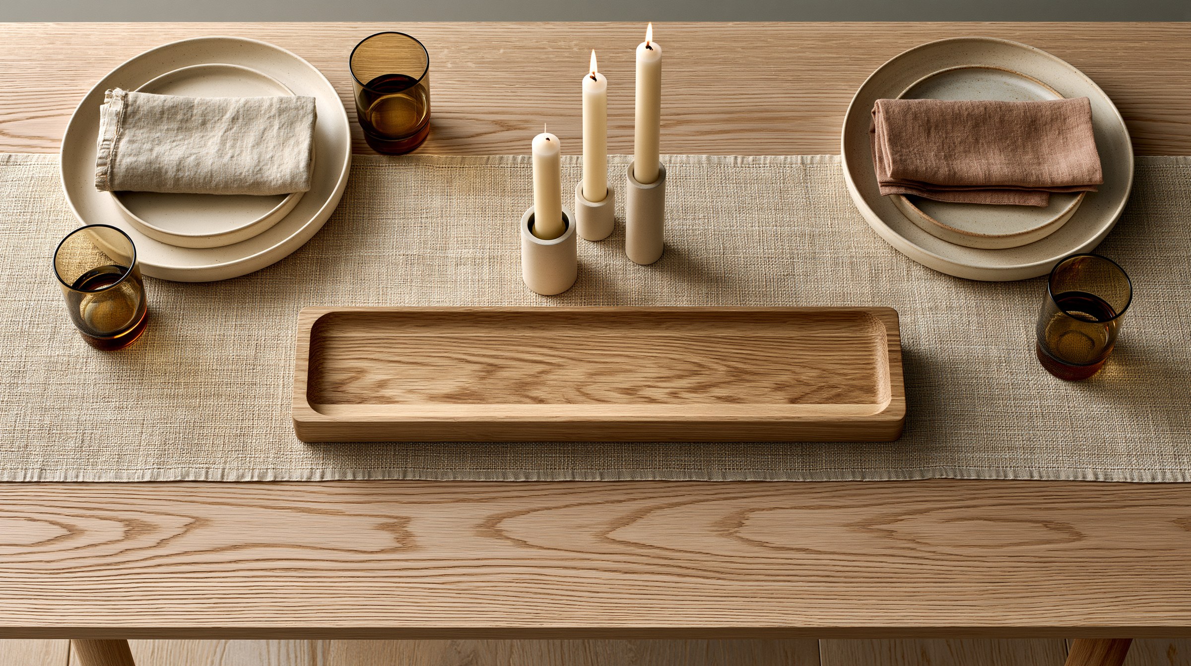 Linen runner and matte stoneware on a light oak table lit by low tapers