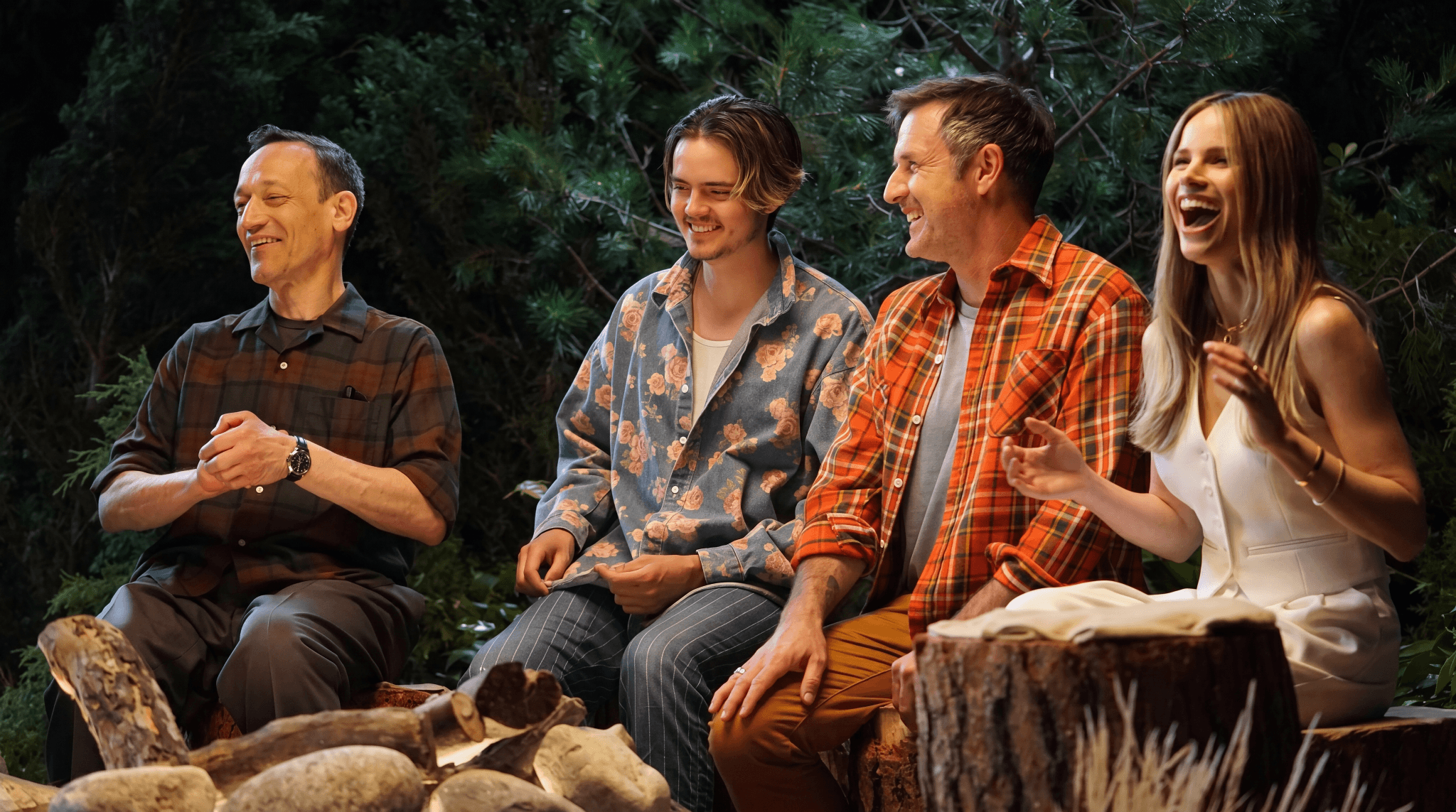 Supermassive Games The Quarry launch party, with four guests laughing around a campfire-style set against woodland scenery