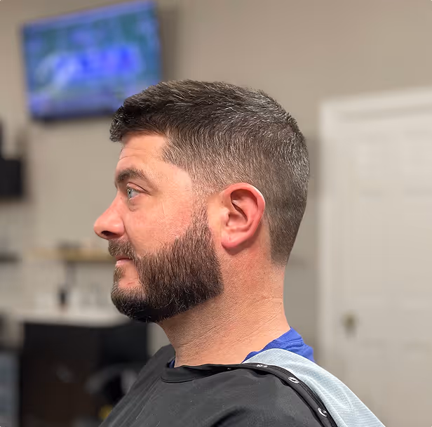 Side profile of a man with a fresh haircut and neatly trimmed full beard in a barbershop.