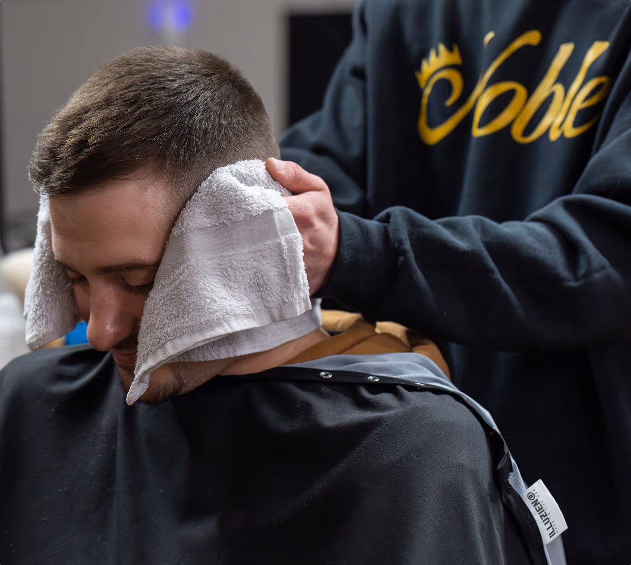 Barber applying warm towel to a man's face during a haircut in a barbershop.