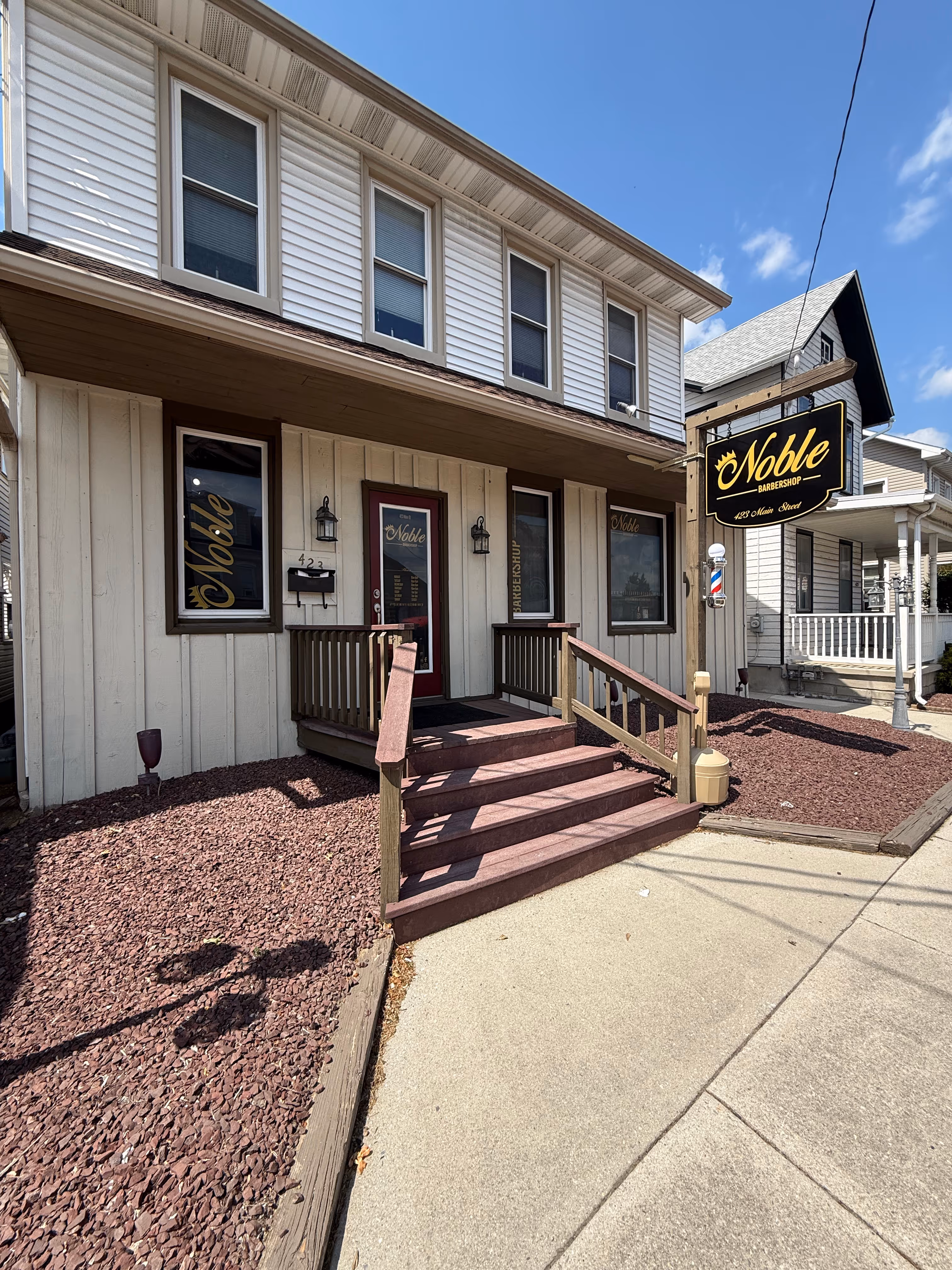 Entrance to Noble Barbershop with stairs, wooden railings, and a hanging black and yellow sign.
