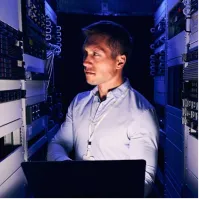 A man in a server room looking at a laptop.