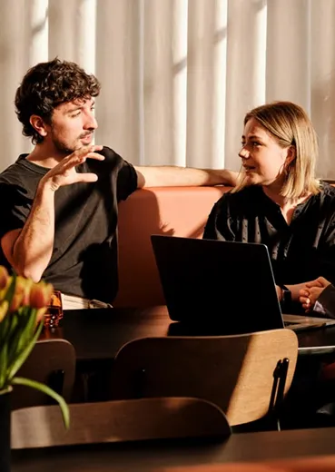 A man and a woman sitting on a couch with laptops.