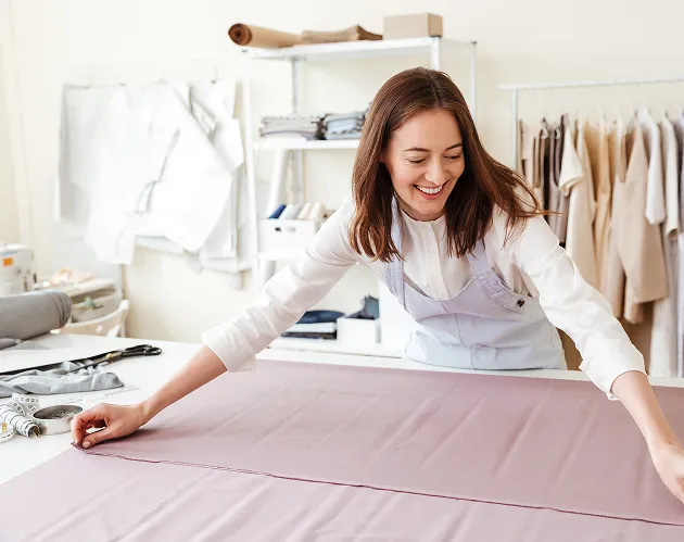 A woman in a white shirt is making a pink piece of cloth.