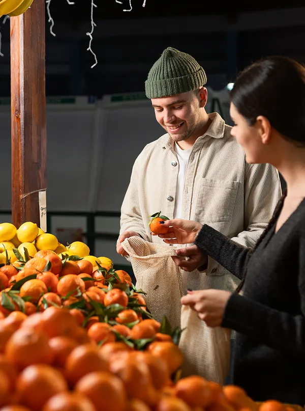 A man and a woman standing in front of a display of oranges.