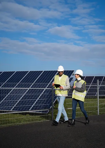 Two people in hard hats standing in front of solar panels.
