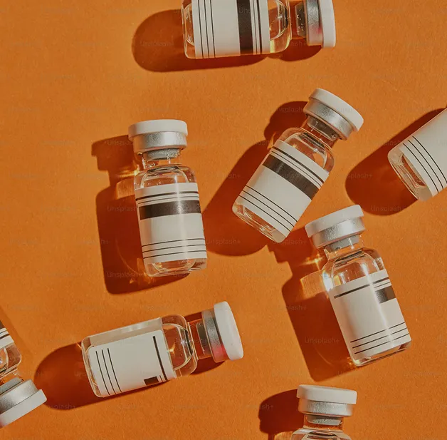 Small clear glass vials with white labels and caps on an orange surface casting shadows.