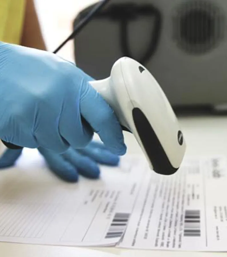 Gloved hand holding a barcode scanner over documents with barcodes on a desk.