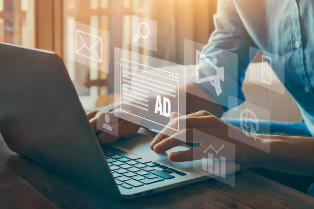 Person typing on a laptop with floating digital icons for advertising and media around the hands.