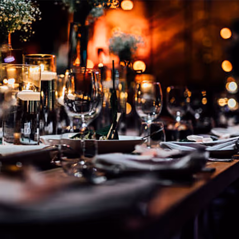 Elegant table setting with wine glasses, candles, and floral centerpieces in dim warm lighting.
