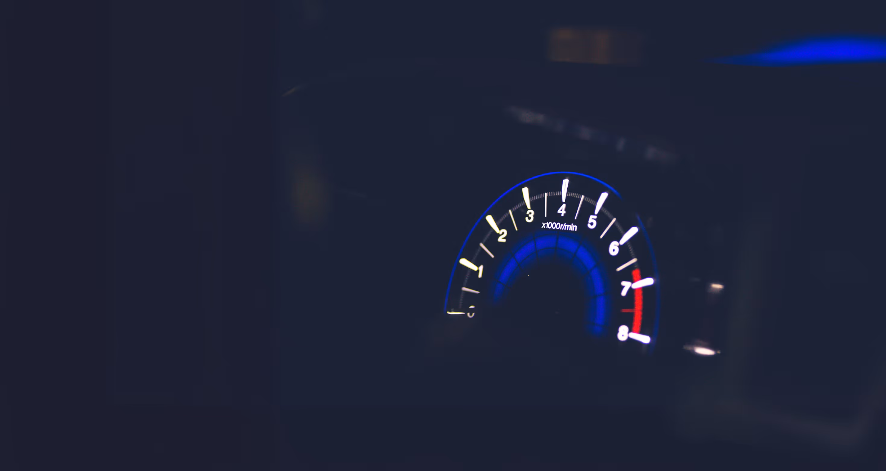 Illuminated car tachometer showing engine speed near 3,000 rpm at night.