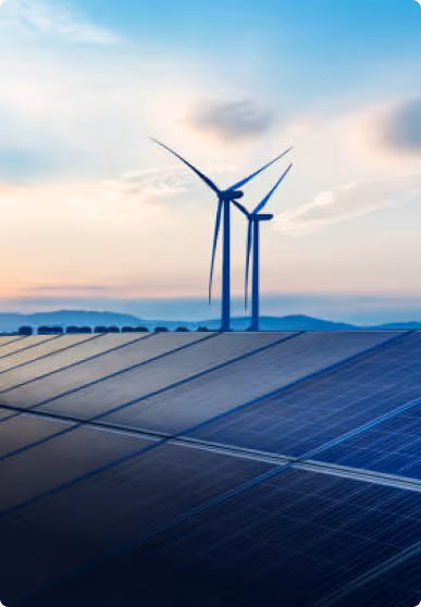 Solar panels in front and two wind turbines with a cloudy sky at sunset in the background.