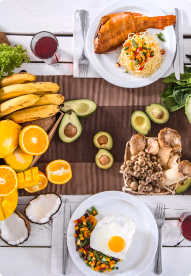 Table set with plates of fried fish and eggs, assorted fruits, vegetables, mushrooms, and glasses of juice.