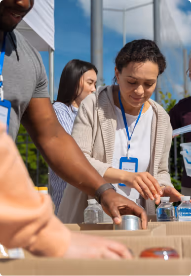 Volunteers sorting canned and bottled goods on a table outdoors under blue sky.