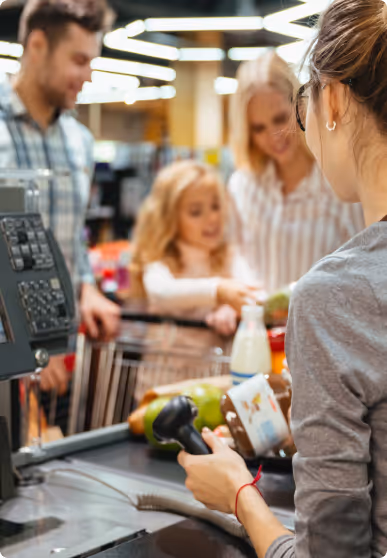 Cashier scanning groceries while a family with a child waits at the checkout counter.