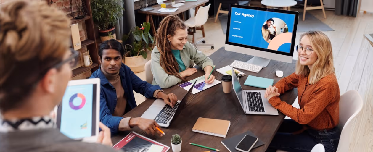 Four colleagues collaborating around a table with laptops and charts in a modern office.