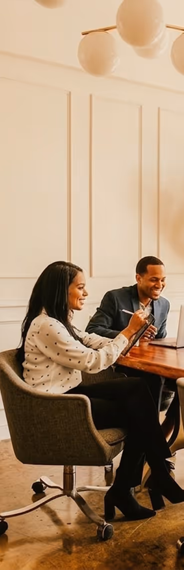 Two businesspeople smiling and working together at a wooden table in a modern office.