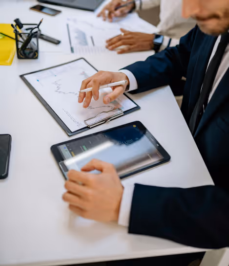 Person in suit analyzing charts on clipboard and tablet during a business meeting.