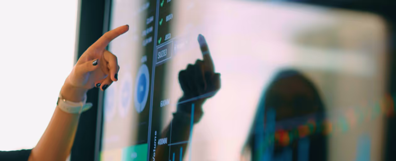Person's hand pointing at a digital touchscreen displaying data charts and graphs.