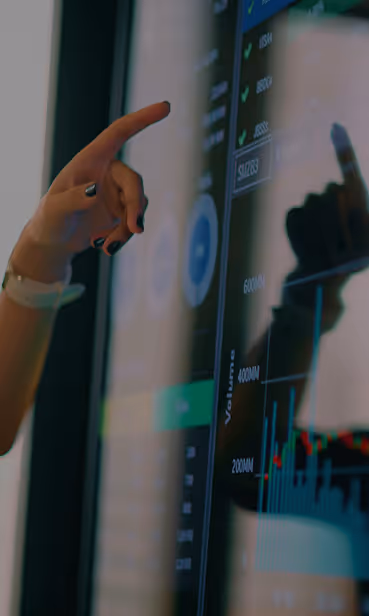 Hand pointing at data charts and graphs on a touchscreen display with financial metrics.